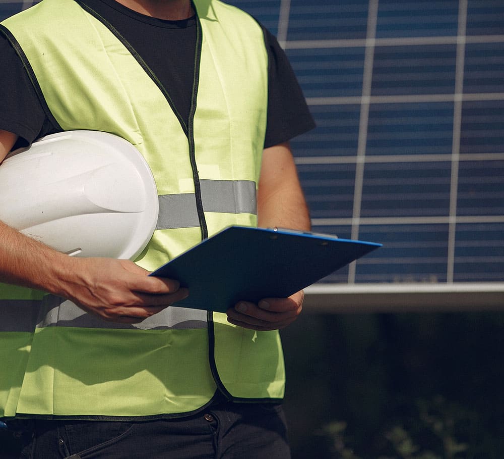 Tecnico con casco e cartellina davanti ai pannelli fotovoltaici.